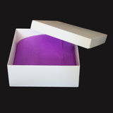 Caja de cartón blanca semiabierta con tapa inclinada, mostrando en su interior papel de seda de color morado. Ideal para empaques personalizados, e-commerce y regalos corporativos.