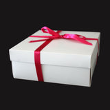 Caja de regalo de cartón blanca cerrada, decorada con una cinta de raso de color fucsia brillante con lazo, aislada sobre fondo negro. Empaque elegante para obsequios y envíos.
