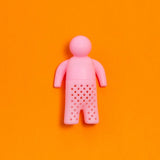 Infusor de té de silicona en forma de figura humana color rosado sobre fondo naranjo.