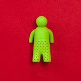 Infusor de té de silicona en forma de figura humana color verde sobre fondo rojo.