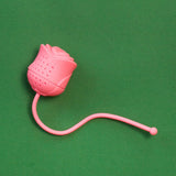 Infusor de té de silicona en forma de rosa color rosado sobre fondo verde.